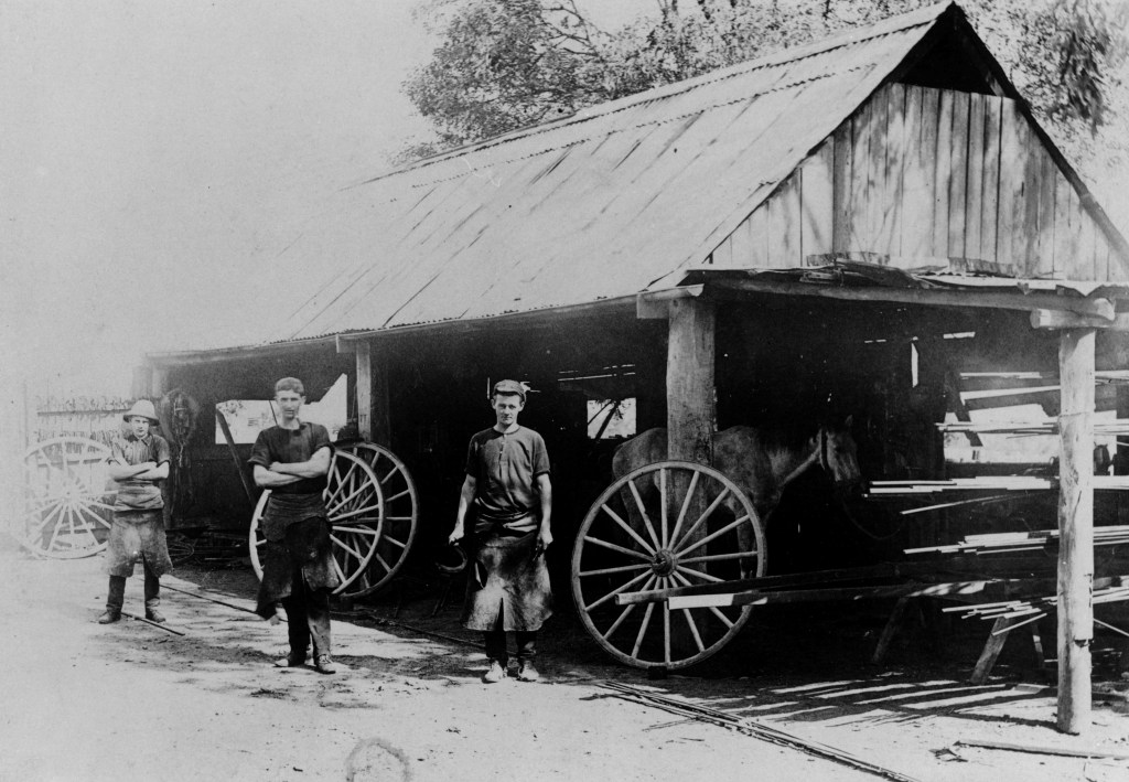 Ted Taylor's blacksmiths shop at Alderley about 1912
Three Blacksmiths posing outside the smithy with wagon wheels in the background.
