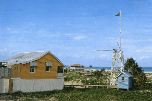 A colourised photograph of the signal station that replaced the Amity Point station. It shows a group of weatherboard buildings occupied by the pilots and their crew, and a flagstaff for signalling ships in the bay.